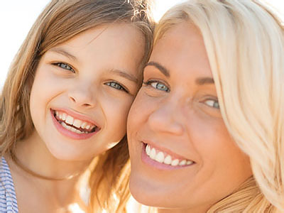 The image shows a woman and a young girl, both smiling and looking at the camera. They appear to be in a happy moment together.