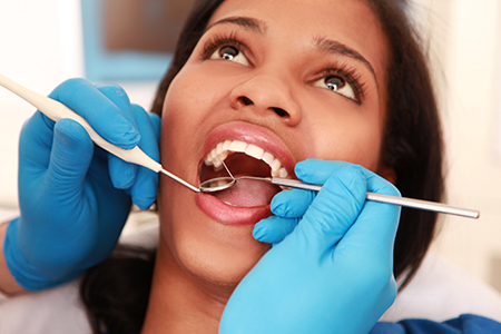 A dental professional performing oral care on a patient, with the patient wearing a blue surgical gown and having their mouth open.